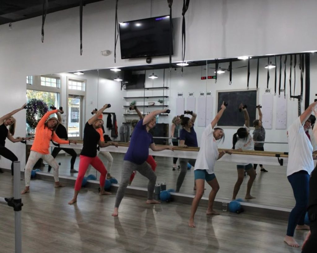 Barre class at Clemson Fitness Company. Class of women lined up at barre, stretching in unison.