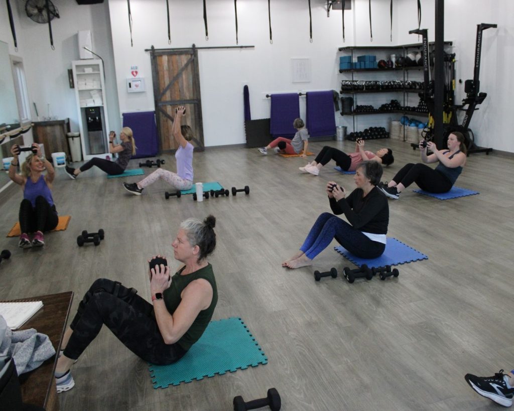 Class of women in CFC sitting on mats, doing crunches with weights.