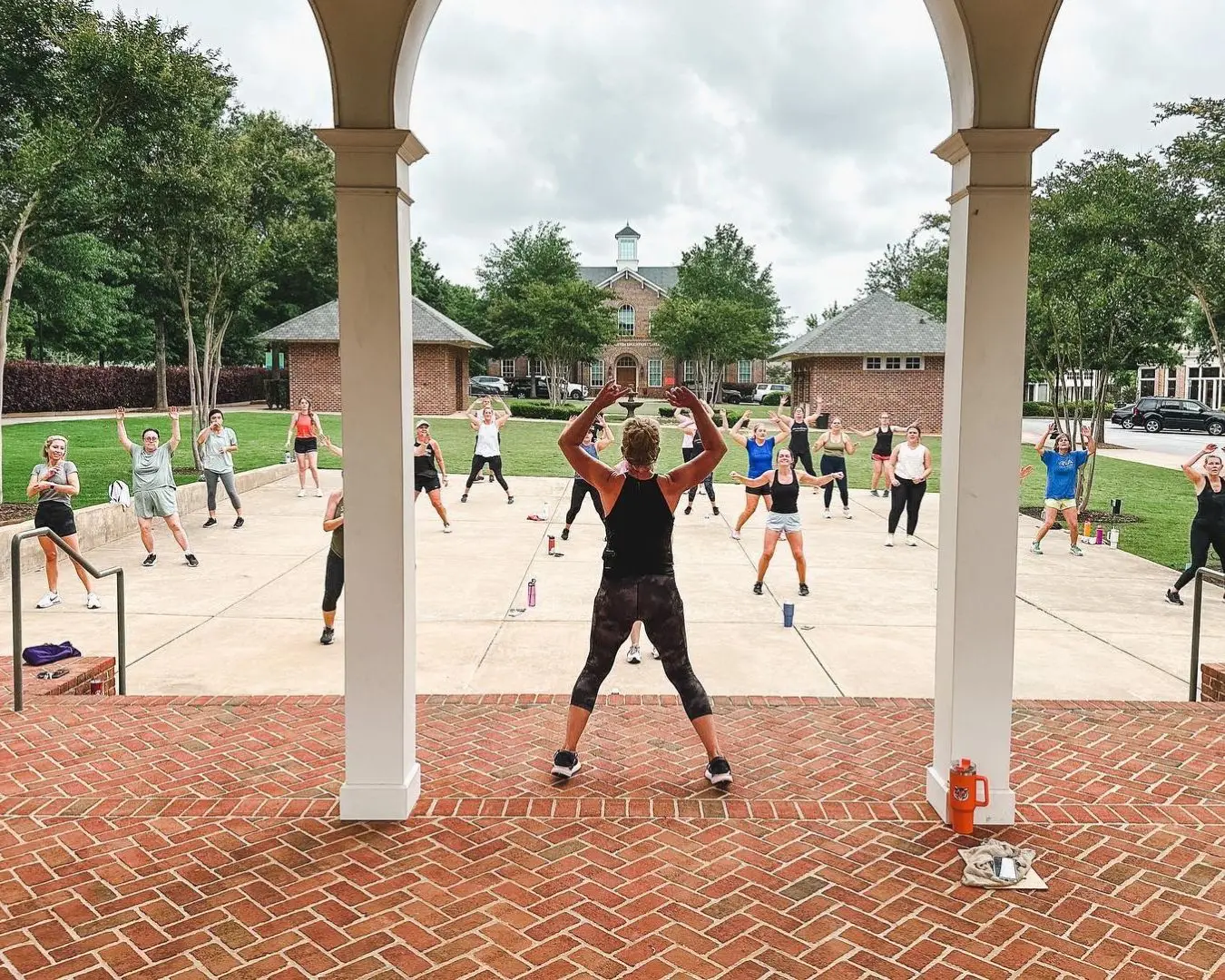 Clemson Fitness class being taught outside during the summer. Shot from behind of female instructor with group of people in front of her following instructions, have fun.
