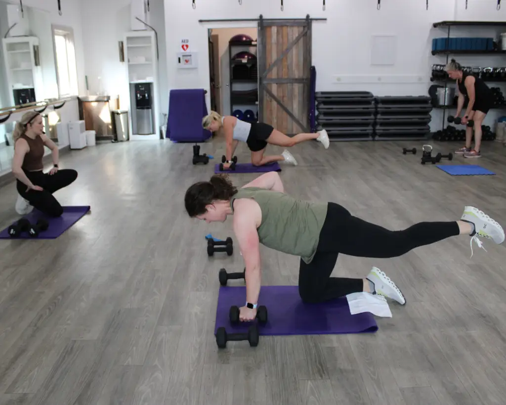 Class at Clemson Fitness where group of women are balancing on knee, holding onto weight, and lifting back leg.
